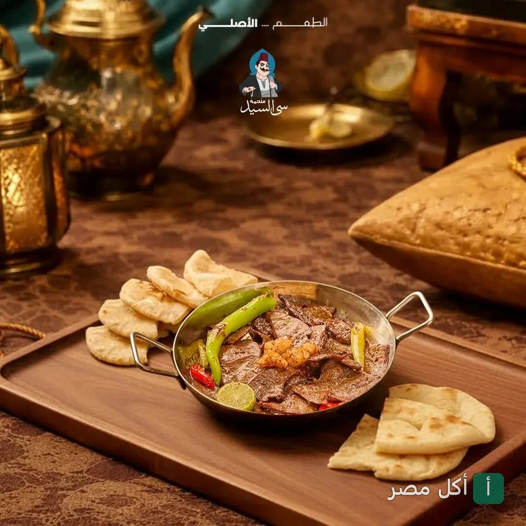 طبق كبدة مصري في مقلاة معدنية مع خبز طازج على طاولة خشبية في مطعم سى السيد بطنطا.