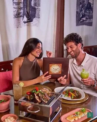 زوجان يطلبان الطعام من قائمة مطعم الخال المصري في القاهرة مع أطباق المشاوي على الطاولة.