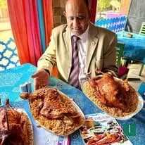 رجل يرتدي بدلة يقدم أطباق من الدجاج المحمر مع الأرز في مطعم تاچوري بالقاهرة.