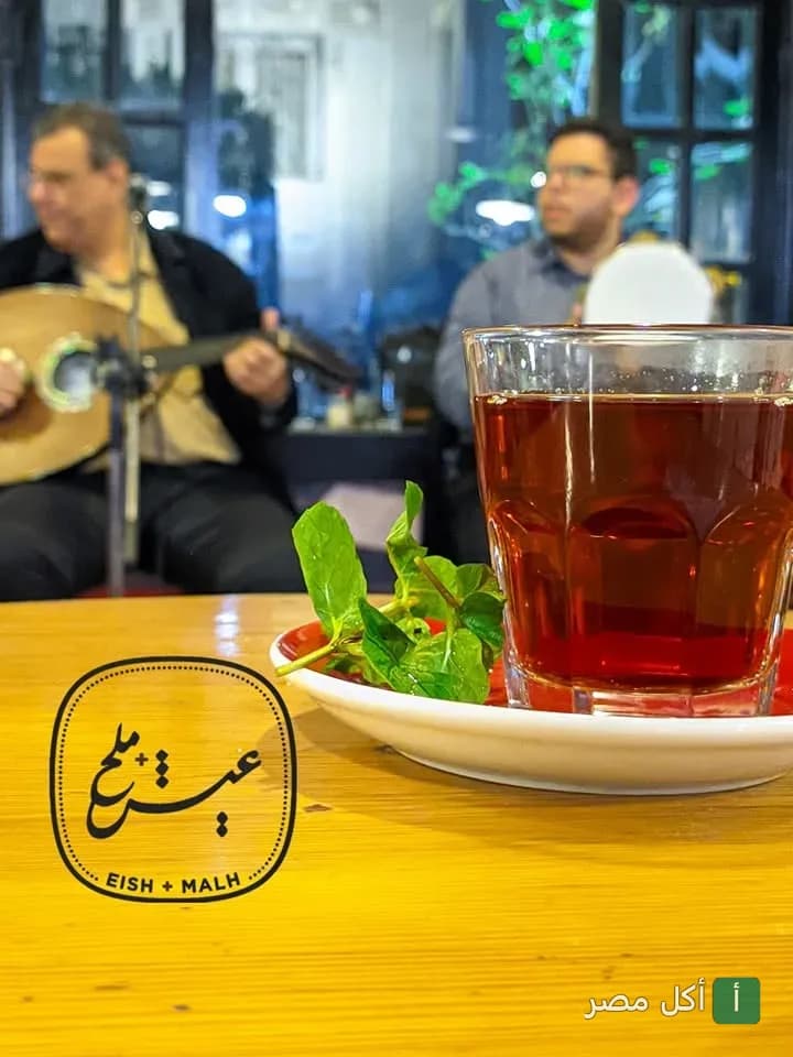 كوب شاي بالنعناع على طاولة في مطعم عيش + ملح بالقاهرة مع موسيقيين يعزفون في الخلفية.