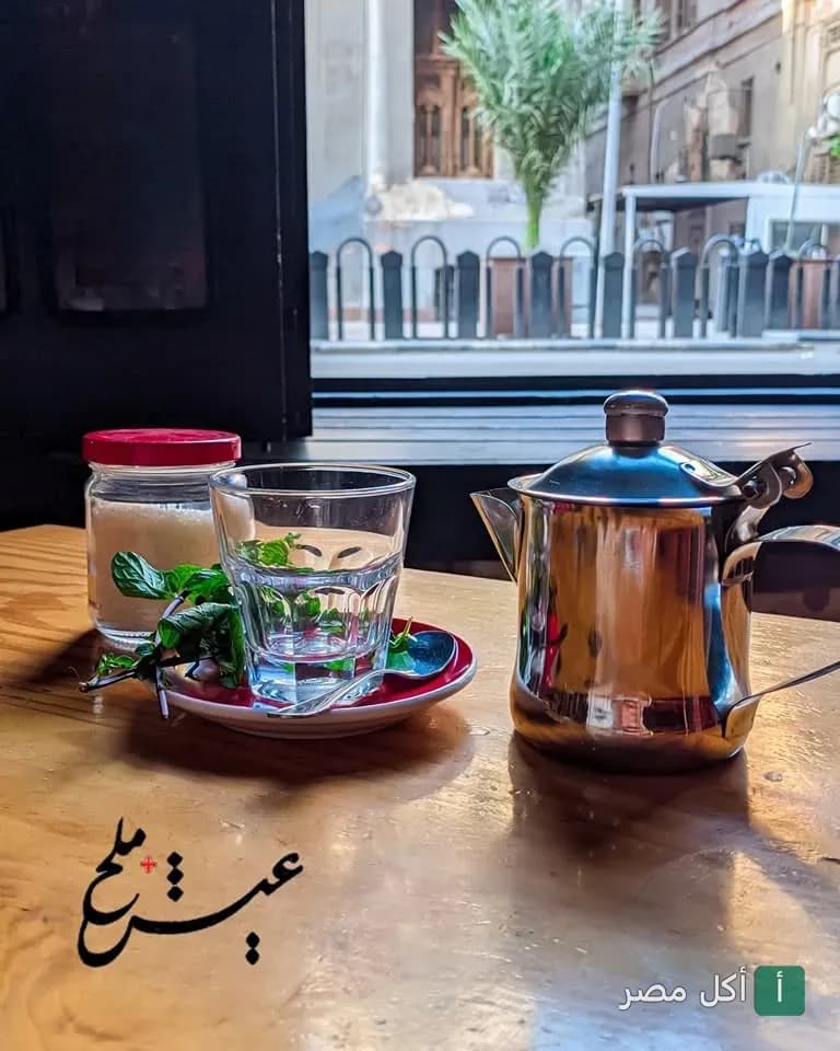 براد شاي وكوب بلمسة نعناع على طاولة خشبية في مطعم عيش + ملح بالقاهرة.