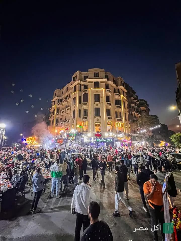 زحام وحيوية أمام مطعم بجه في القاهرة ليلاً مع إضاءة المبنى التاريخي.