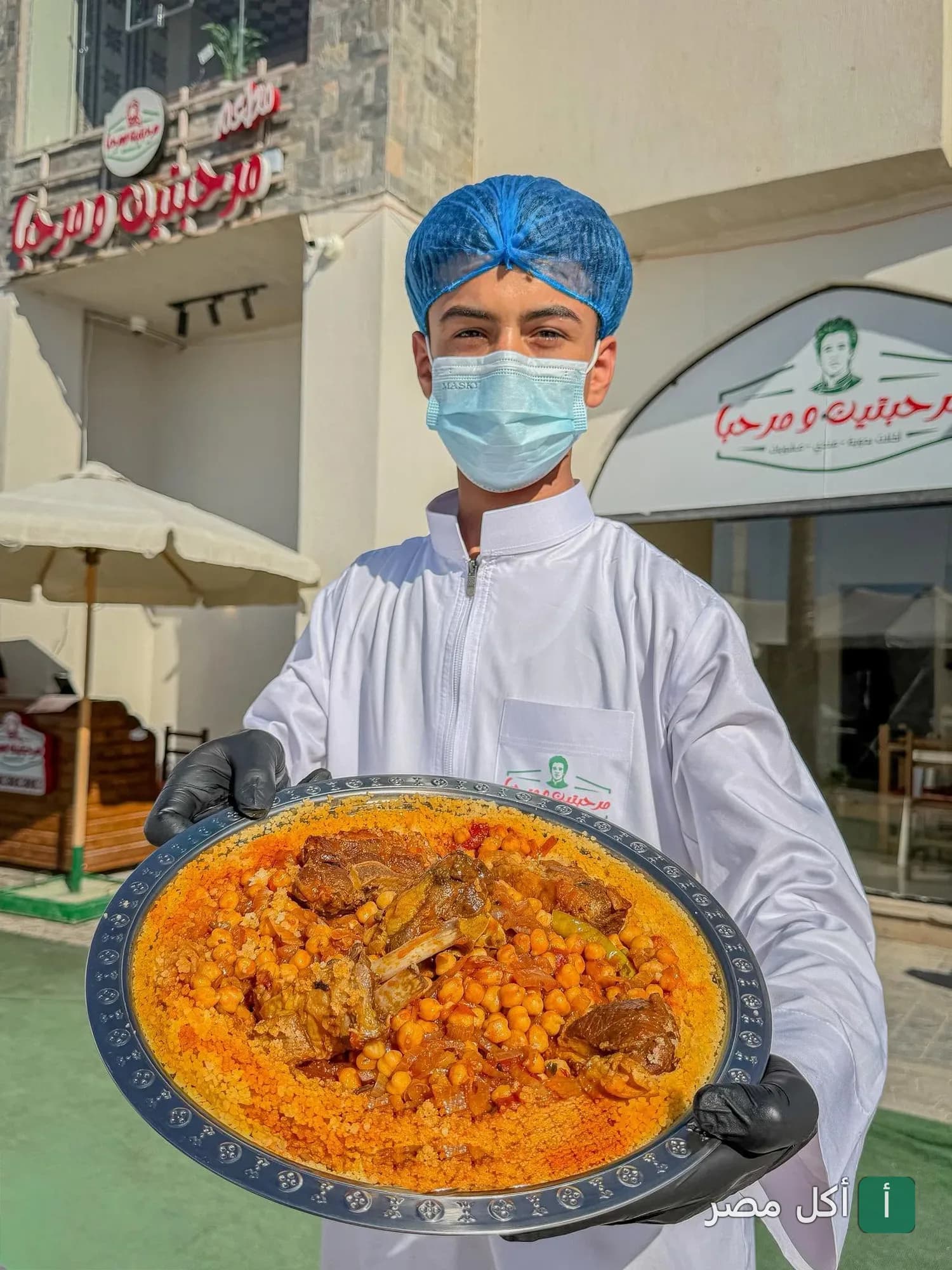 موظف مطعم مرحبتين ومرحبا في مارينا العلمين يقدم صينية كسكسي باللحم والحمص.