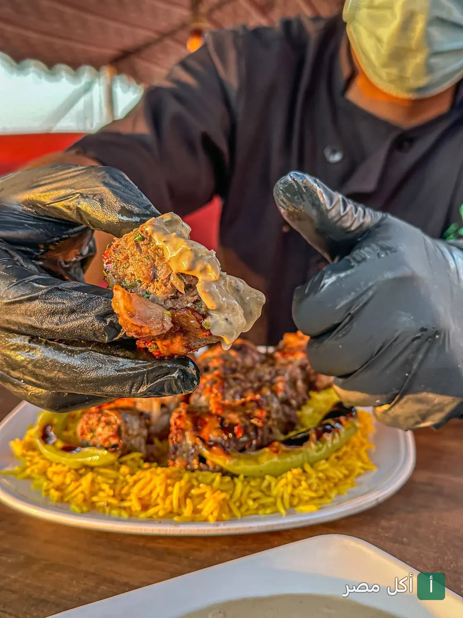 شيف يرتدي قفازات سوداء يقدم طبق مشاوي مع أرز في مطعم مرحبتين ومرحبا بمارينا العلمين.