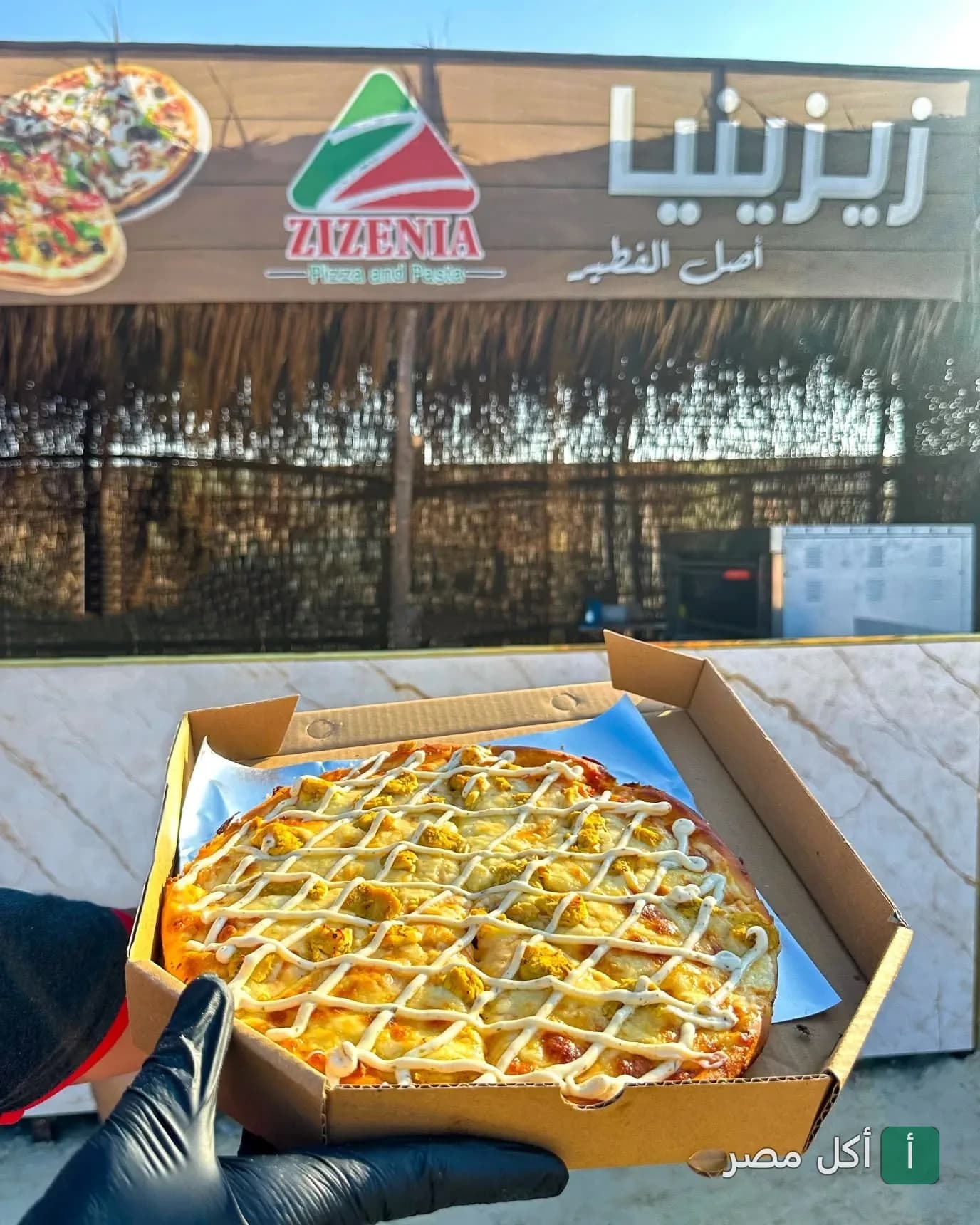 بيتزا زيزينيا في مارينا العلمين تقدم بيتزا طازجة في علبة كرتون أمام واجهة المطعم.