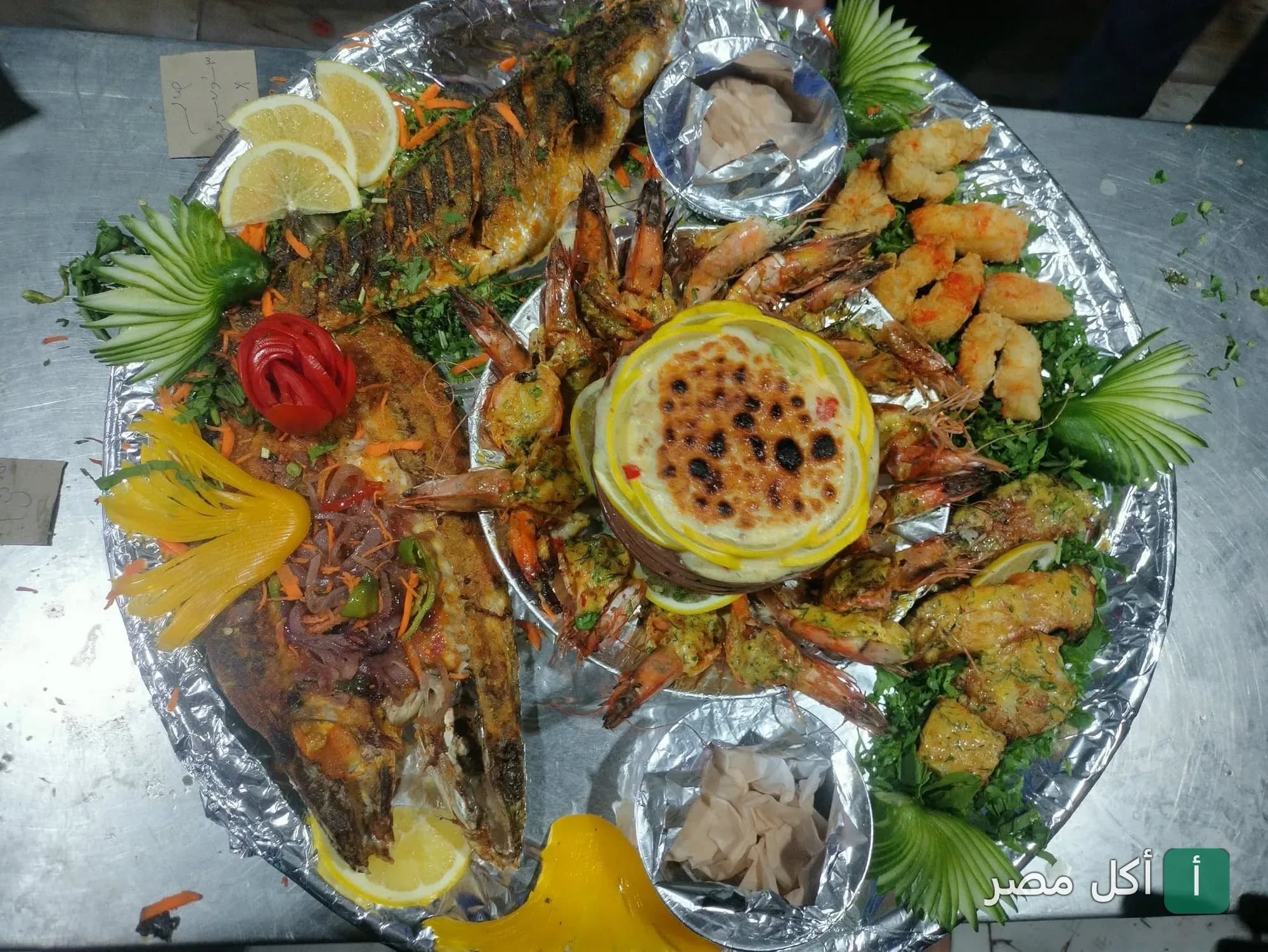 طبق مأكولات بحرية مشكلة من مطعم دحروج في مارينا العلمين، يضم سمك مشوي وجمبري وطاجن بحري مزين بالخضروات.