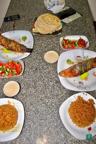 سفرة مأكولات بحرية في مطعم استاكوزا بمنيا القمح، تشمل سمك مشوي، أرز صيادية، سلطة خضراء، وطحينة مع خبز.