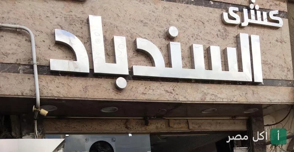 واجهة مطعم كشري السندباد في منيا القمح، تظهر لافتة المطعم المعدنية البارزة.