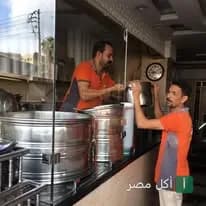موظفان بزي برتقالي يجهزان أطباق الكشري داخل مطعم كشري السندباد في منيا القمح.