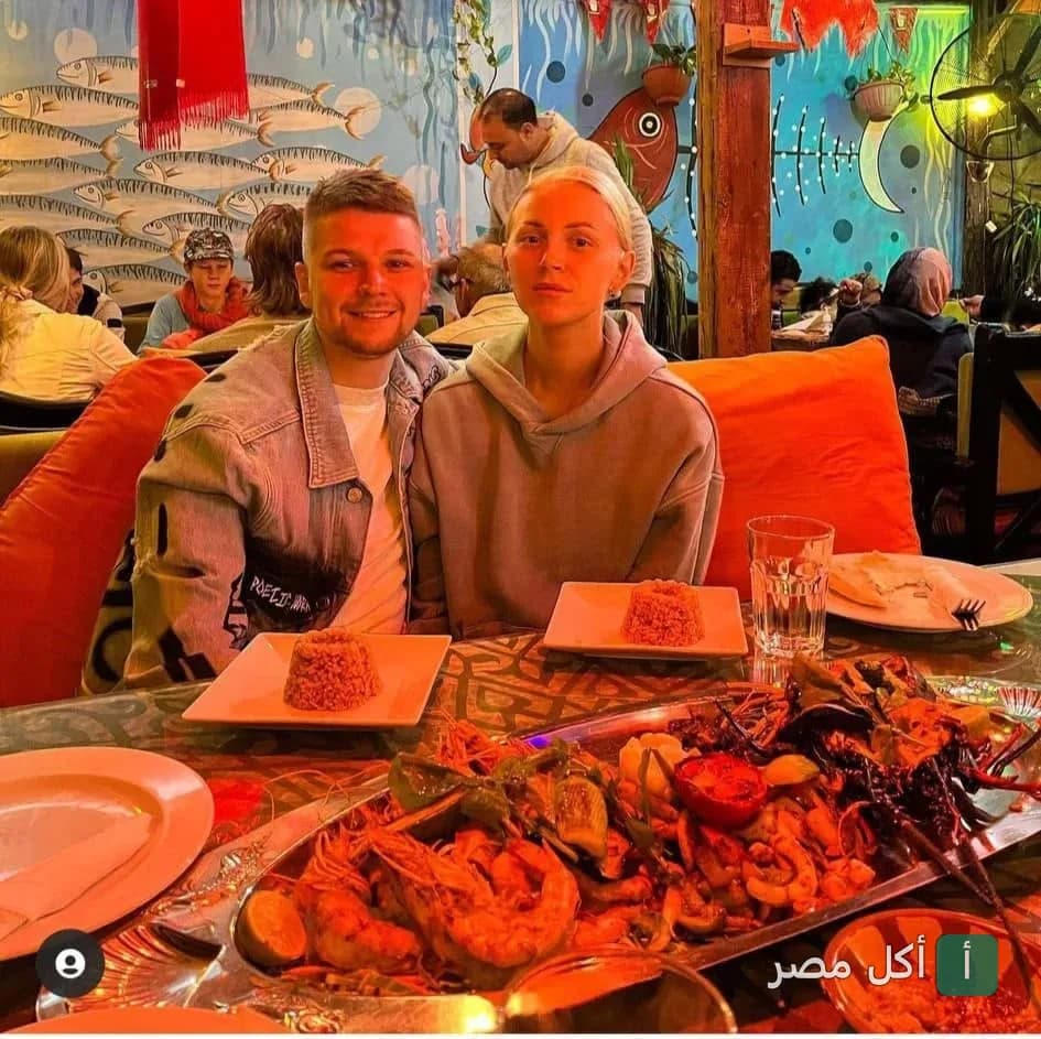 زوجان يتناولان وجبة مأكولات بحرية متنوعة في مطعم شارك دهب وسط ديكورات بحرية ملونة.