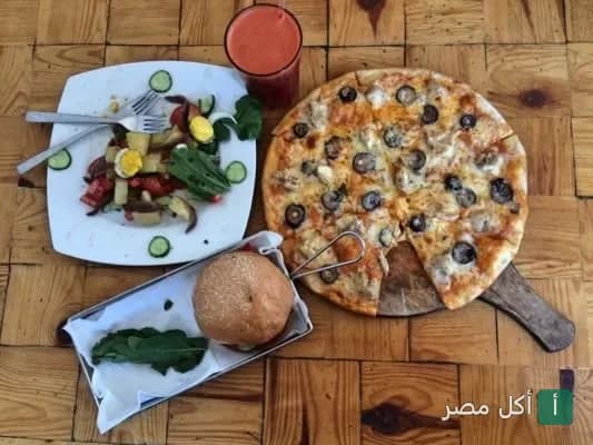 بيتزا بالزيتون وسلطة وبرجر على طاولة خشبية في مطعم أثانور بيتزيريا بدهب.