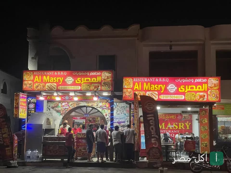 واجهة مطعم المصري للمشاوي في دهب ليلاً مع لافتات حمراء مضيئة وزبائن أمام المطعم.