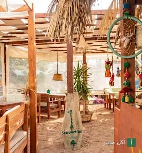 جلسة خارجية بديكور بوهيمي في مطعم سيادكشن دهب مع أرضية رملية وديكورات خشبية.