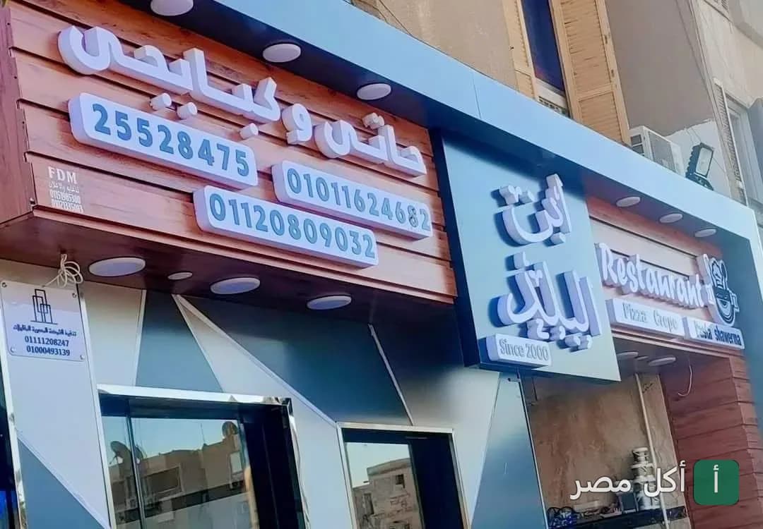 واجهة مطعم كبابجي ابن البلد في مدينة 15 مايو، يظهر اسم المطعم وأرقام التواصل على لافتة خشبية حديثة.