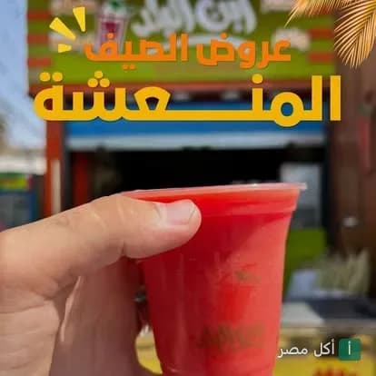 كوب عصير أحمر منعش في يد شخص أمام واجهة مطعم كبابجي ابن البلد في مدينة 15 مايو.