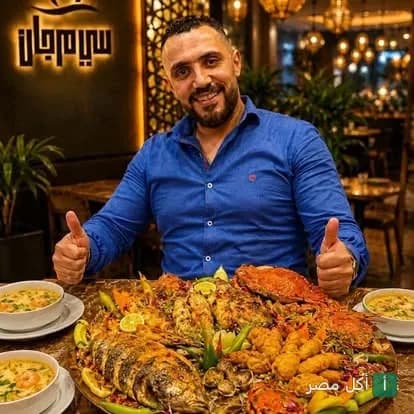 رجل يبتسم أمام صينية مأكولات بحرية متنوعة في مطعم سي مرجان بمدينة 15 مايو.
