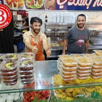 موظفو مطعم عم بشندي في 15 مايو يبتسمون خلف واجهة عرض تحتوي على أطباق الفول والفلافل الجاهزة.