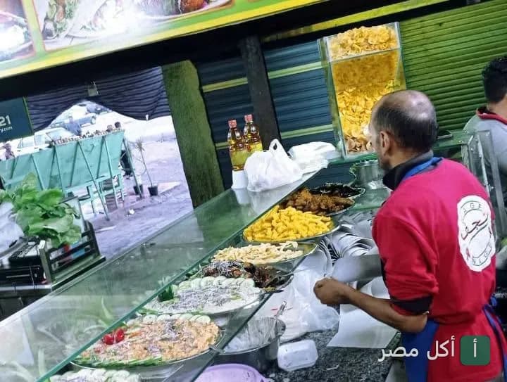 موظف في مطعم نجف بمدينة 15 مايو يجهز الطلبات أمام واجهة عرض تحتوي على تشكيلة من المقبلات والمأكولات.