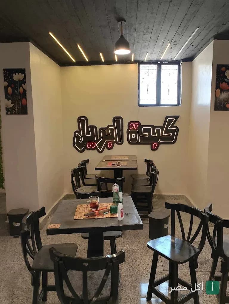 جلسة داخلية في مطعم كبدة إبريل بمدينة 15 مايو مع شعار المطعم المضيء على الحائط.