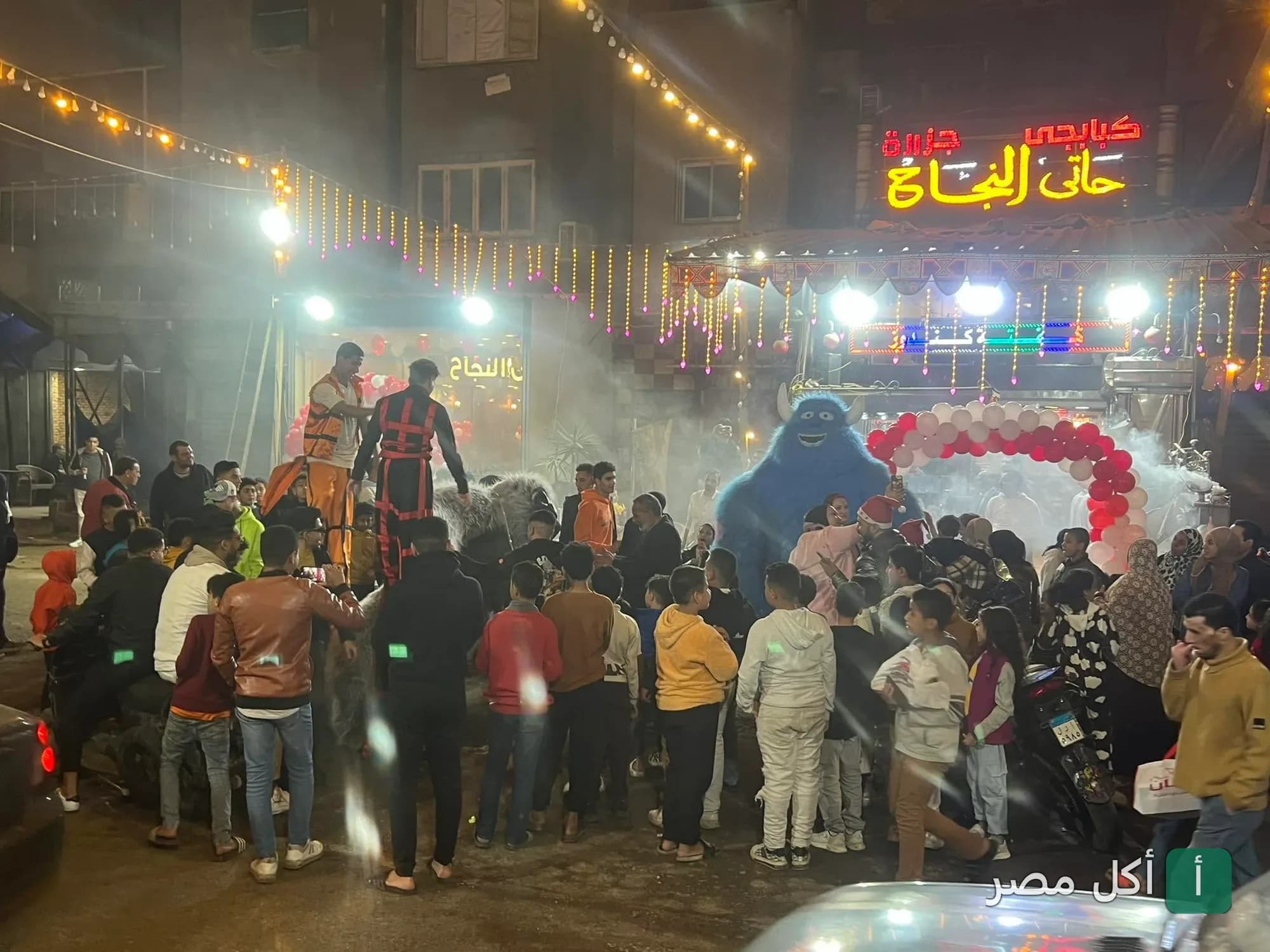 احتفالية أمام مطعم النجاح للمأكولات الشرقية في الأزبكية مع عروض ترفيهية وأضواء زينة.