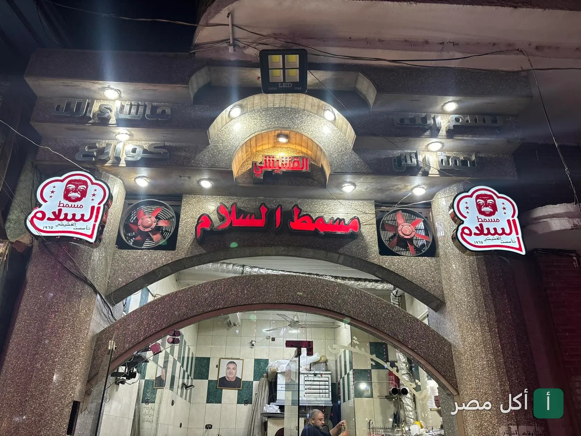 واجهة مطعم القشيشي في الأزبكية ليلاً، تظهر لافتة مسمط السلام المضيئة وتصميم المدخل الحجري.