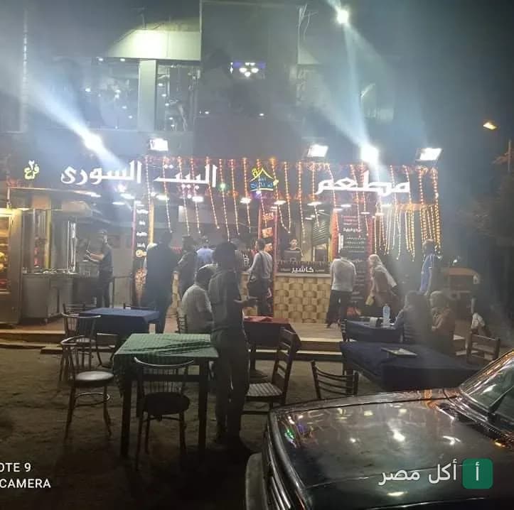 واجهة مطعم البيت السوري في البساتين ليلاً مع جلسات خارجية مضيئة.