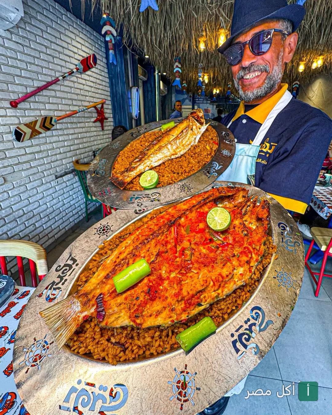 موظف في مطعم بهيج بالإسكندرية يقدم أطباق سمك مشوي مع أرز الصيادية في صالة الطعام.