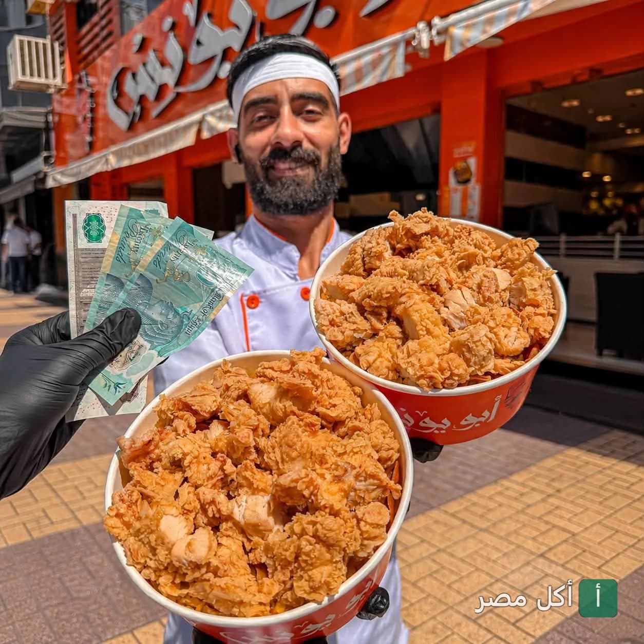 موظف مطعم أبو يونس في البيطاش بالإسكندرية يحمل وجبتين من الدجاج المقرمش أمام واجهة المطعم.