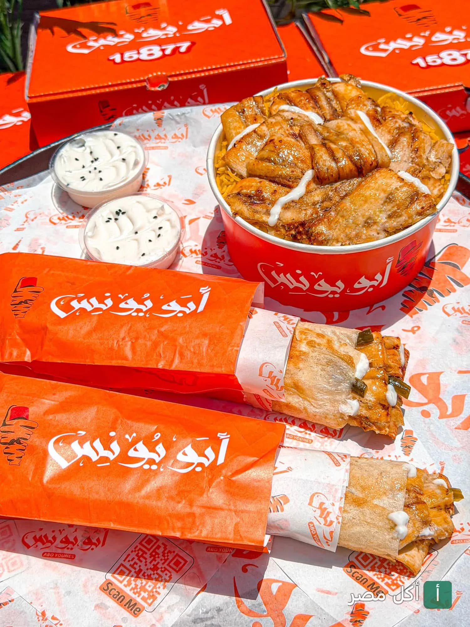 وجبات سريعة من مطعم أبو يونس في البيطاش، تشمل علب أرز بالدجاج وساندوتشات في تغليف المطعم المميز.