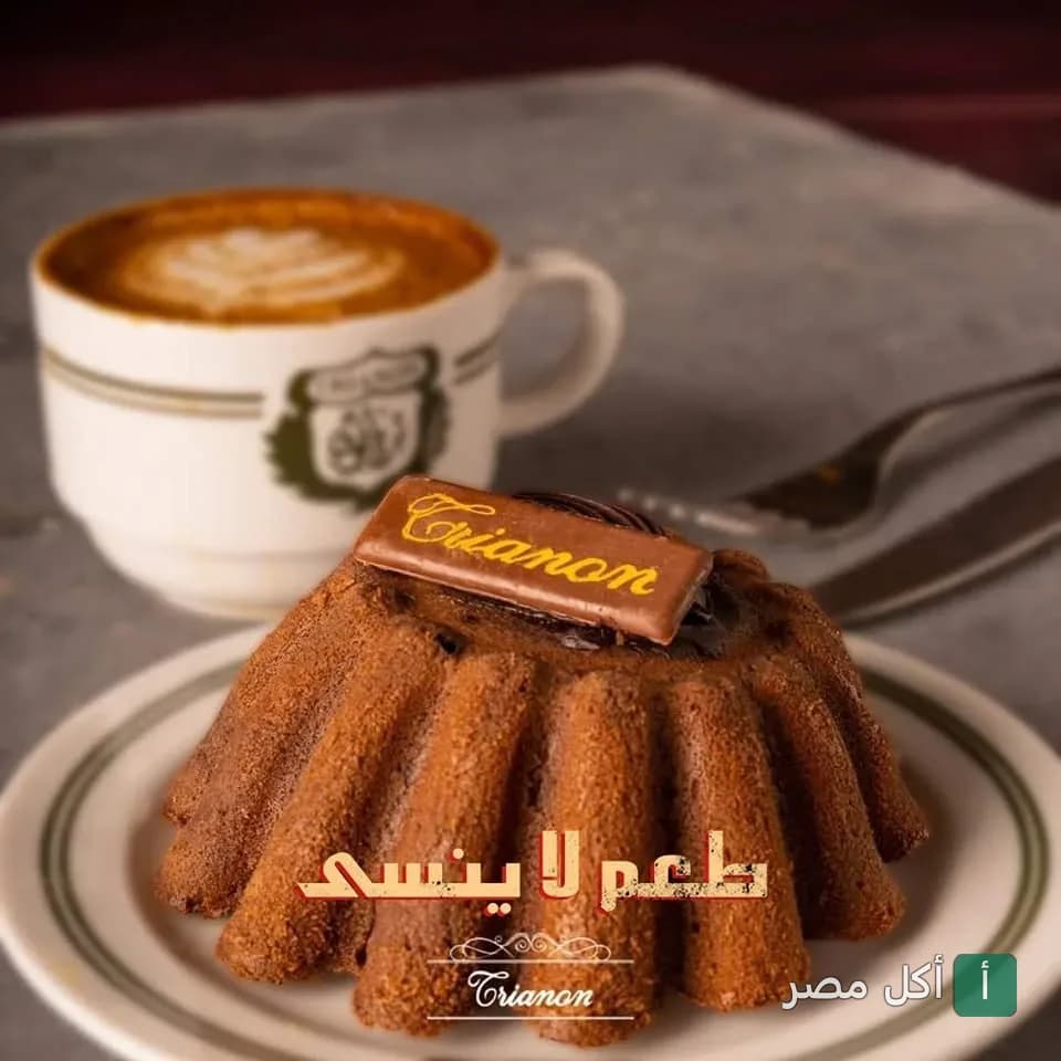 قطعة كيك شوكولاتة مزينة بشعار تريانون مع كوب قهوة في كافيه تريانون بالإسكندرية