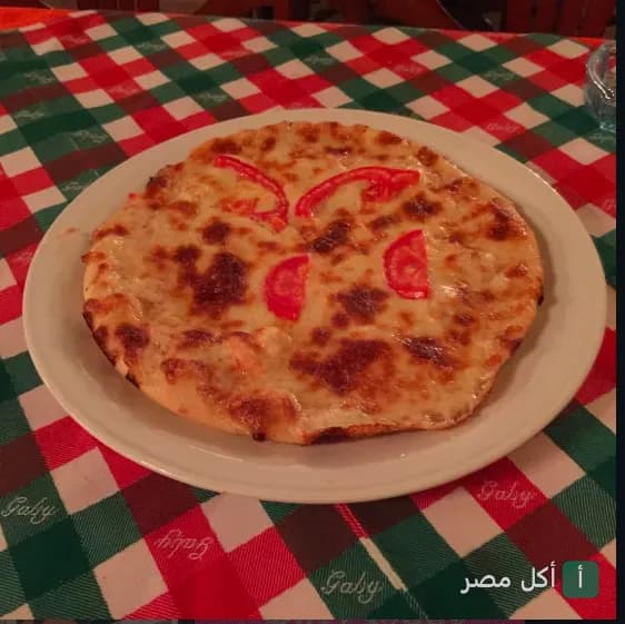 بيتزا بالجبنة والطماطم على مفرش طاولة كاروهات في مطعم شاي غاابي بالعطارين، الرمل.
