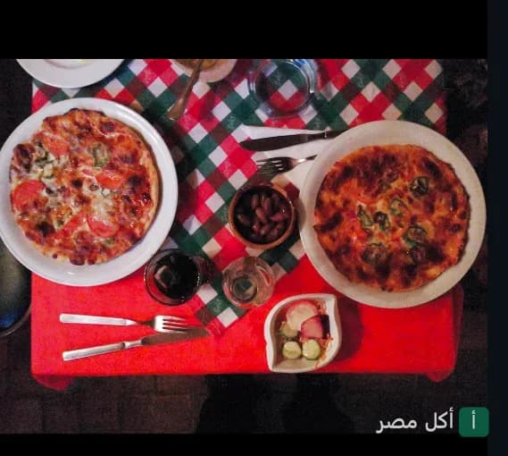 بيتزا متنوعة مع مقبلات على طاولة مغطاة بمفرش كاروهات في مطعم شاي غاابي أو ريتروفو بالعطارين.