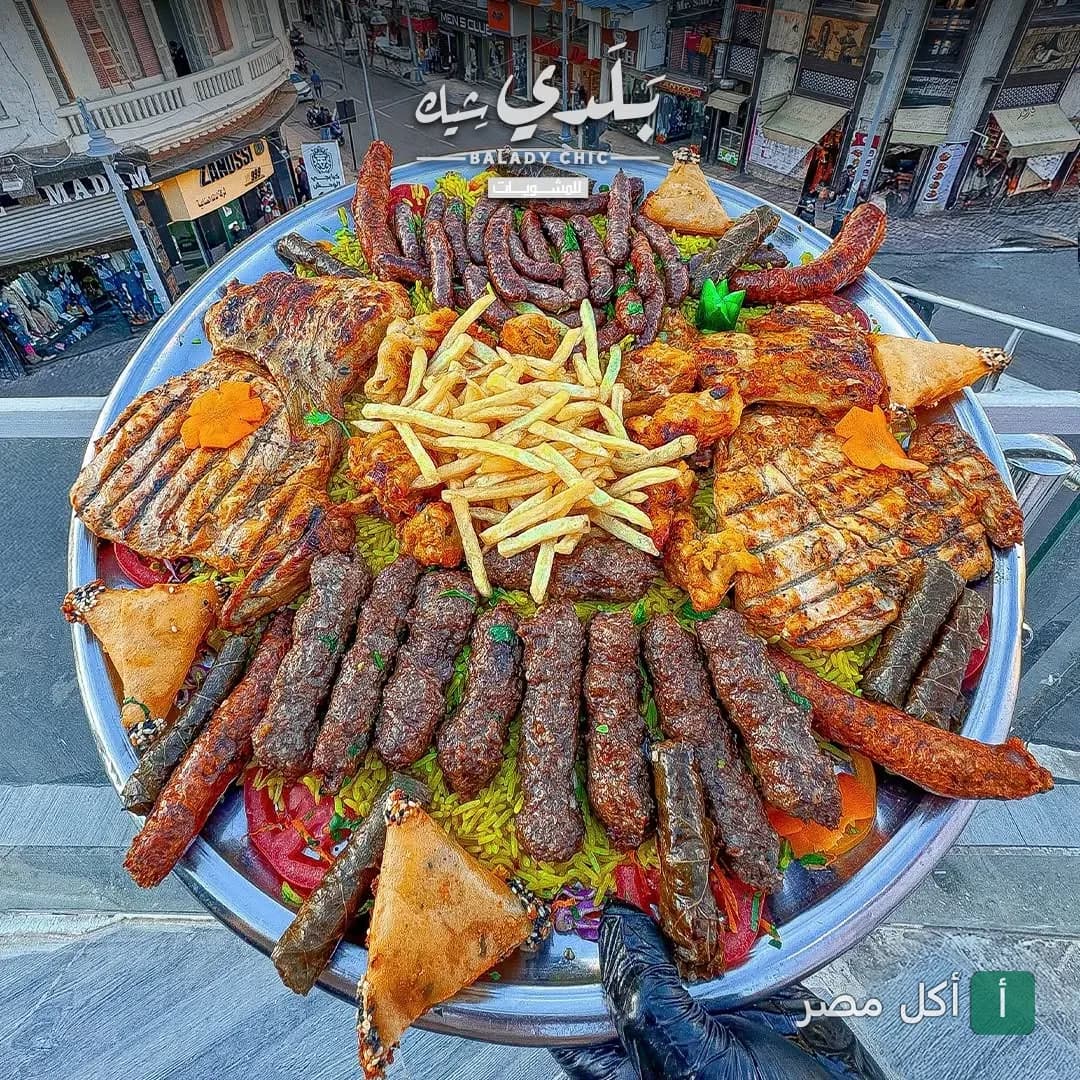 صينية مشاوي مشكلة من مطعم بلدي شيك في الرمل، تحتوي على كفتة وسجق وفراخ مشوية مع أرز وبطاطس محمرة.