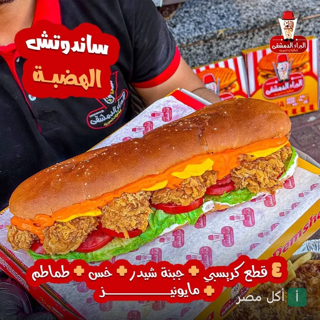 ساندوتش دجاج كرسبي طويل من مطعم البراء الدمشقي 2 في العامرية، محضر بالخس والطماطم وجبنة الشيدر والمايونيز.