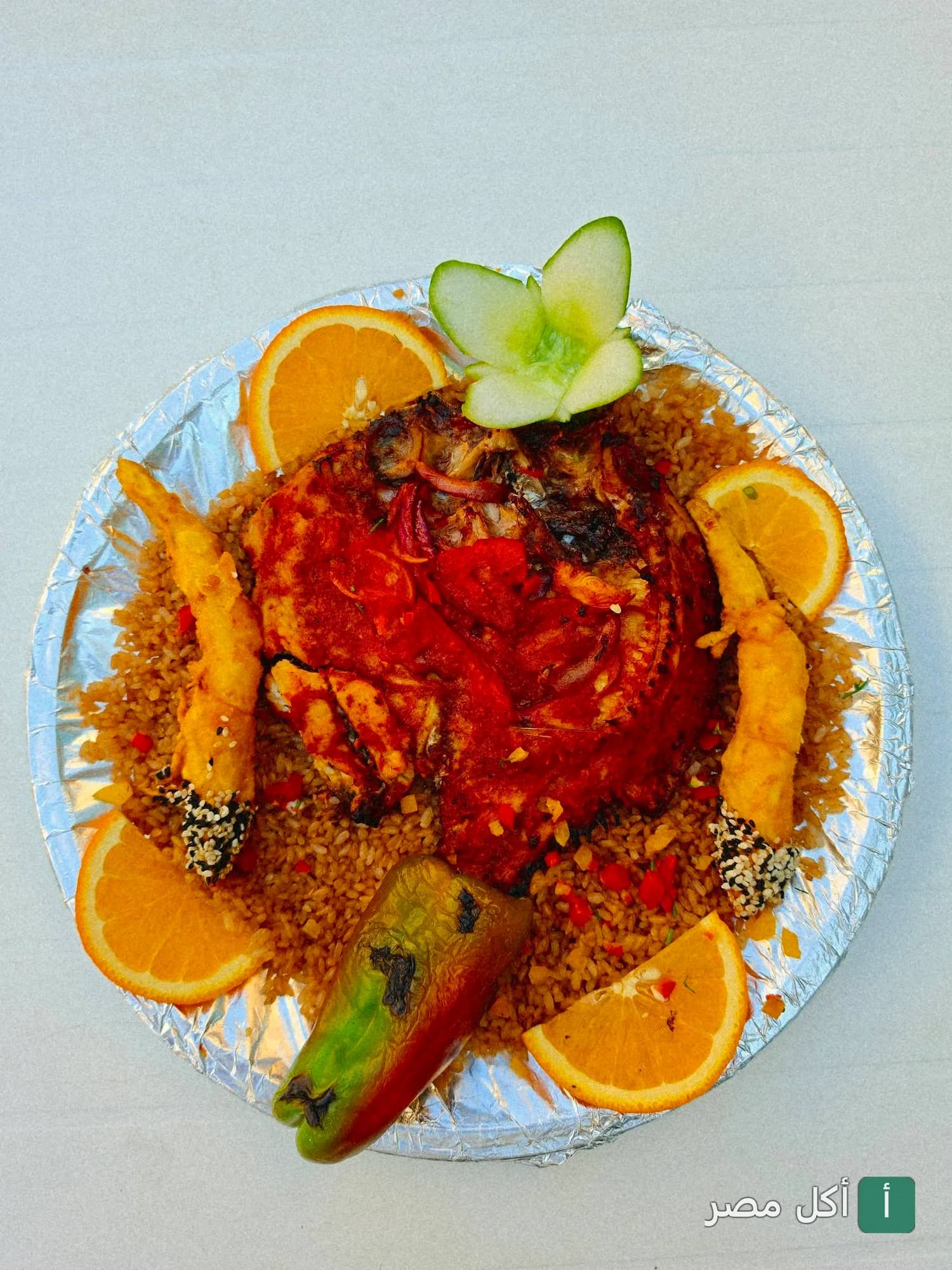 طبق سمك مشوي مع أرز ومأكولات بحرية مزين بالبرتقال في مطعم أسماك الزفر بالعامرية.