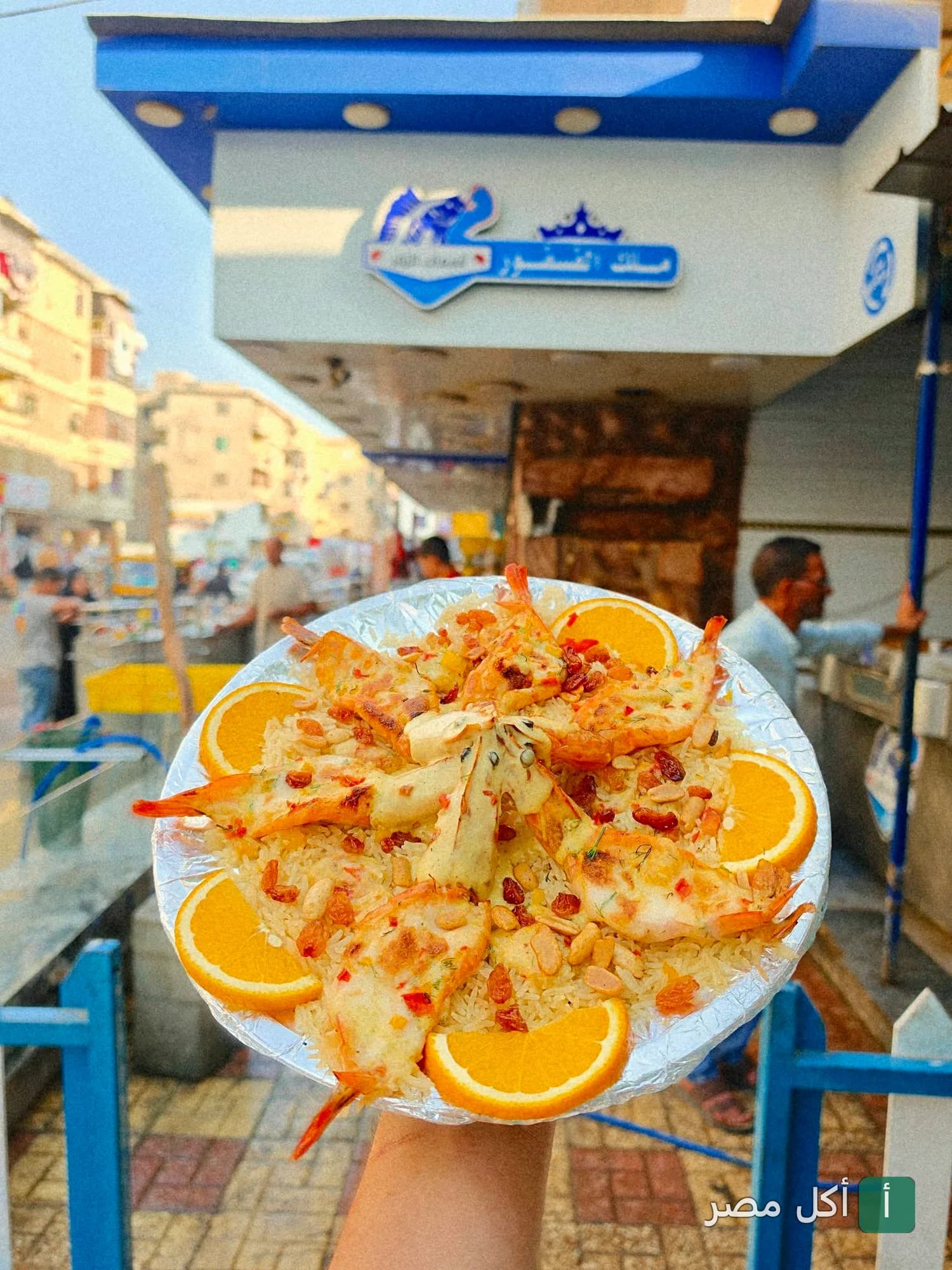 طبق أرز بالجمبري والمكسرات وشرائح البرتقال أمام واجهة مطعم أسماك الزفر في العامرية بالإسكندرية.