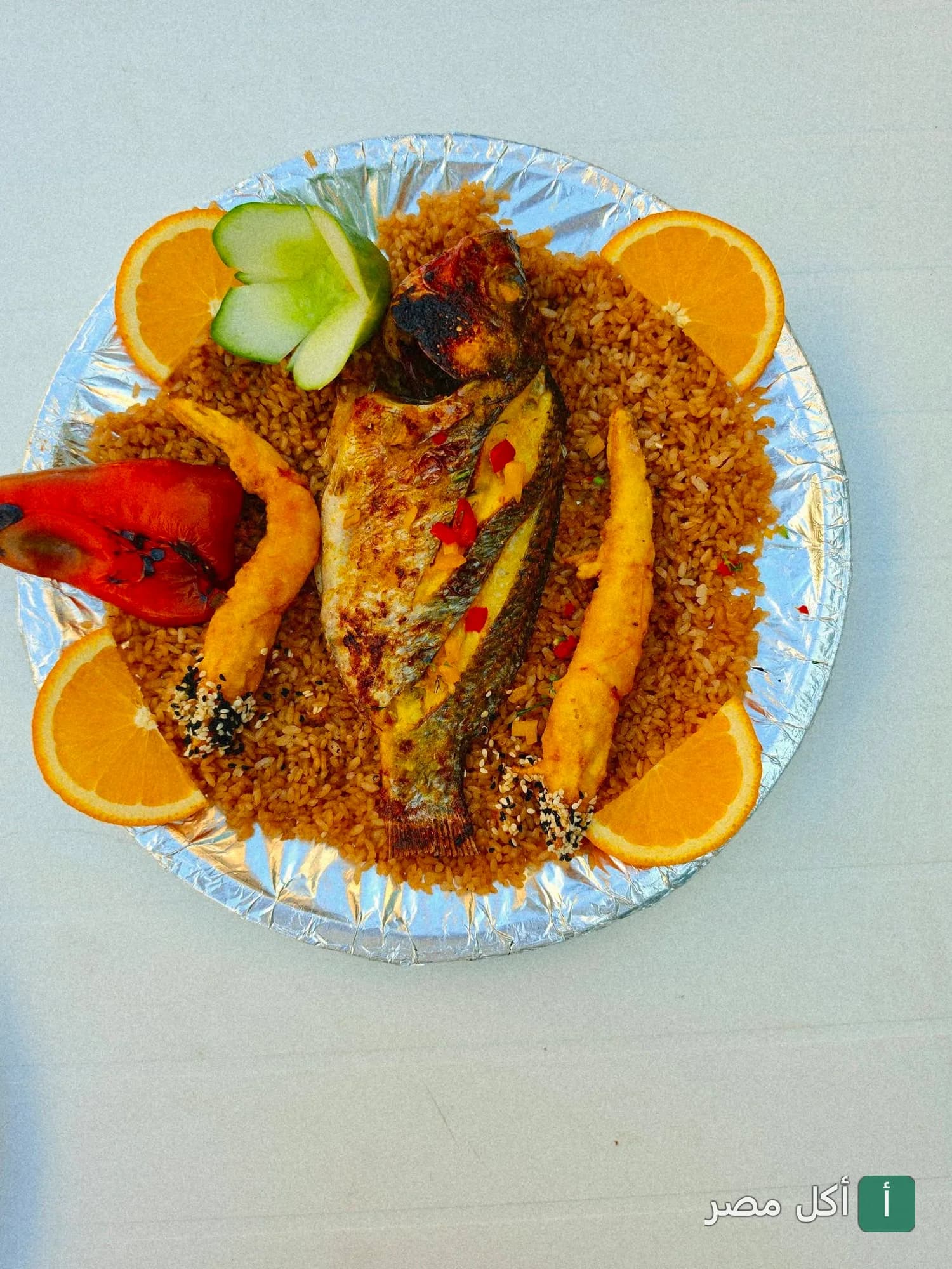 طبق سمك مشوي مع أرز صيادية وجمبري مقلي ومزين بشرائح البرتقال من مطعم أسماك الزفر في العامرية.