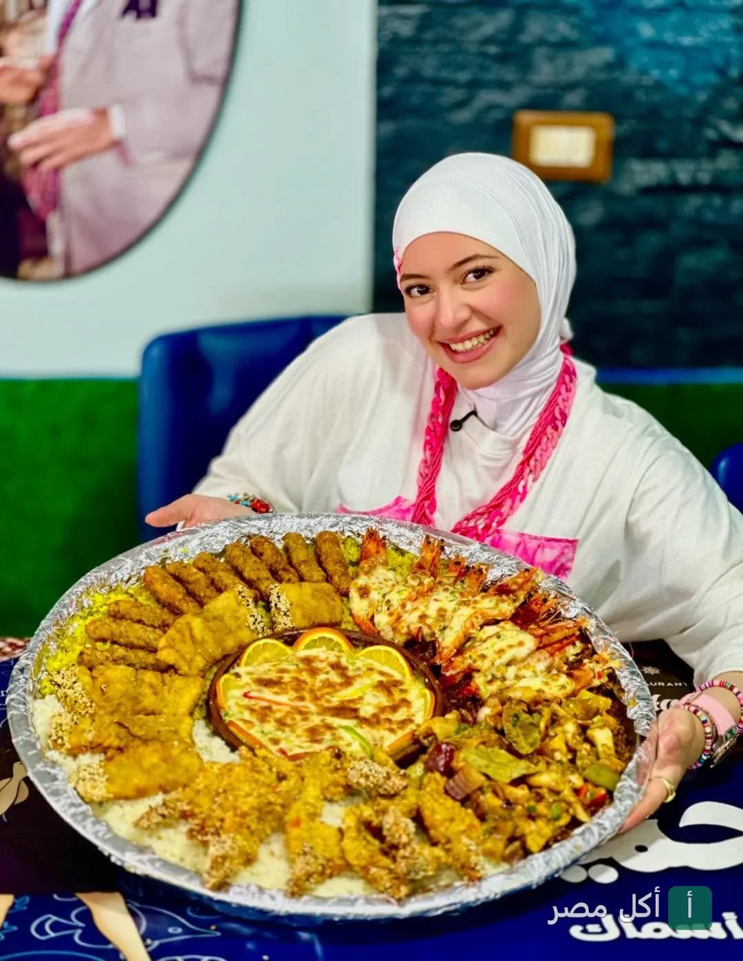 فتاة محجبة تقدم صينية كبيرة متنوعة من المأكولات البحرية والمشاوي في مطعم أسماك ابن حميدو ببور فؤاد.