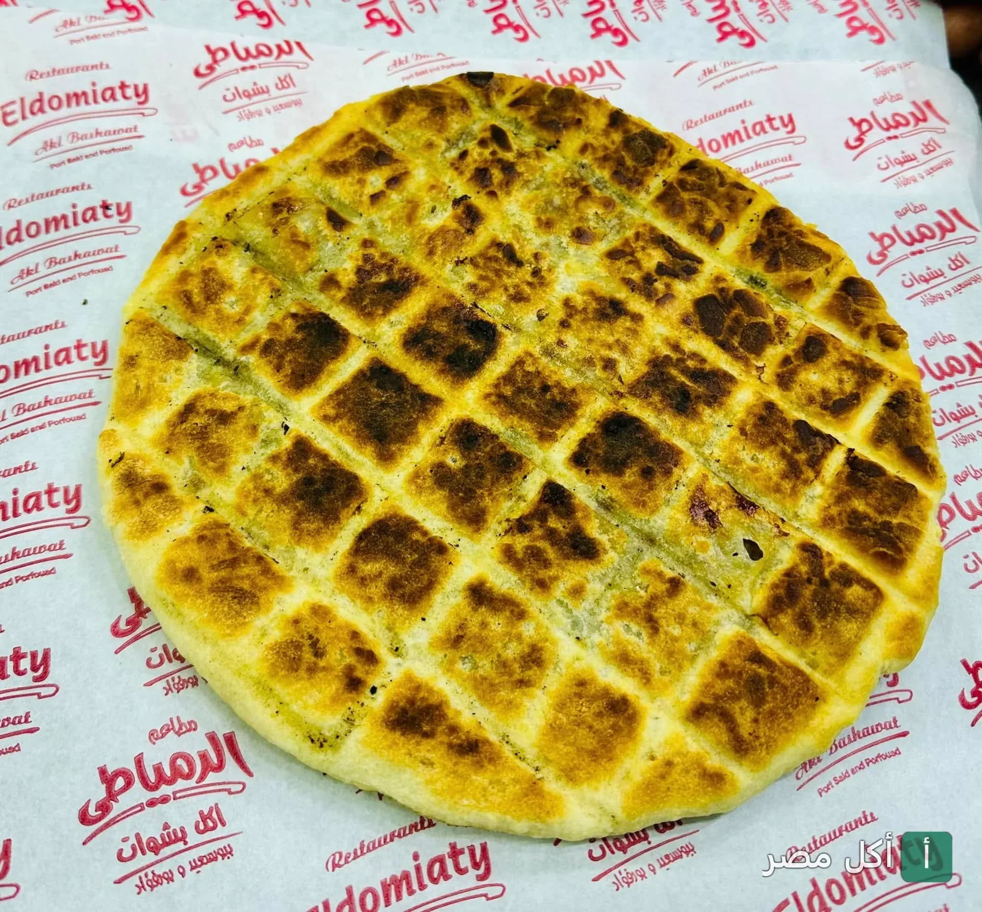 فطيرة محمرة ومقطعة مربعات على ورق تغليف مطعم الدمياطي في بور فؤاد.