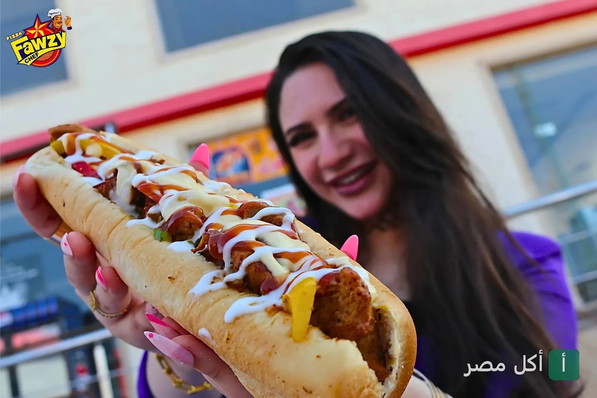 شخص يحمل ساندوتش طويل مغطى بالصوص في مطعم بيتزا فوزي شيف ببورسعيد.