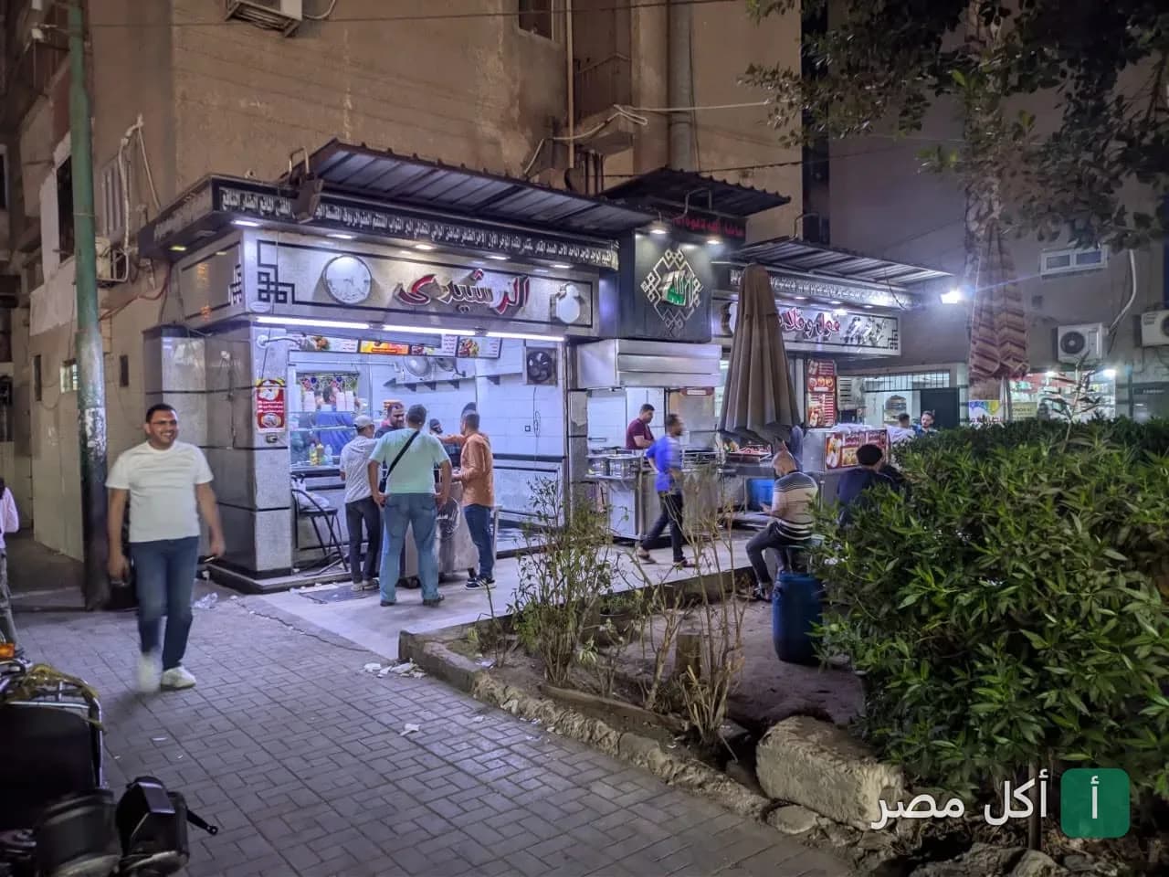 واجهة مطعم الرشيدي في منطقة الزهور ببورسعيد ليلاً مع وجود زبائن أمام المطعم.