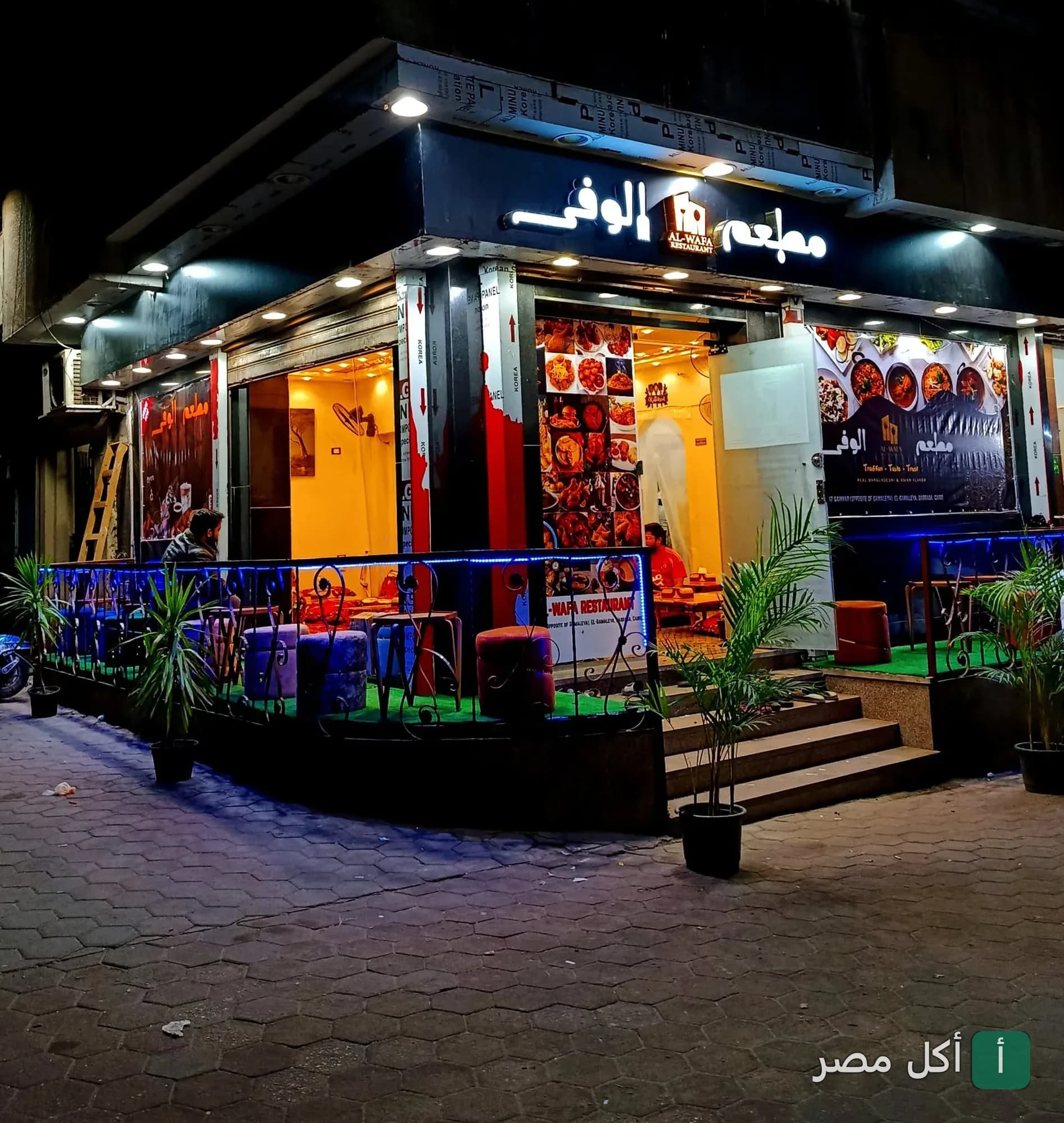 واجهة مطعم الوفى في منطقة الدراسة بالجمالية ليلاً مع إضاءة خارجية وجلسات.