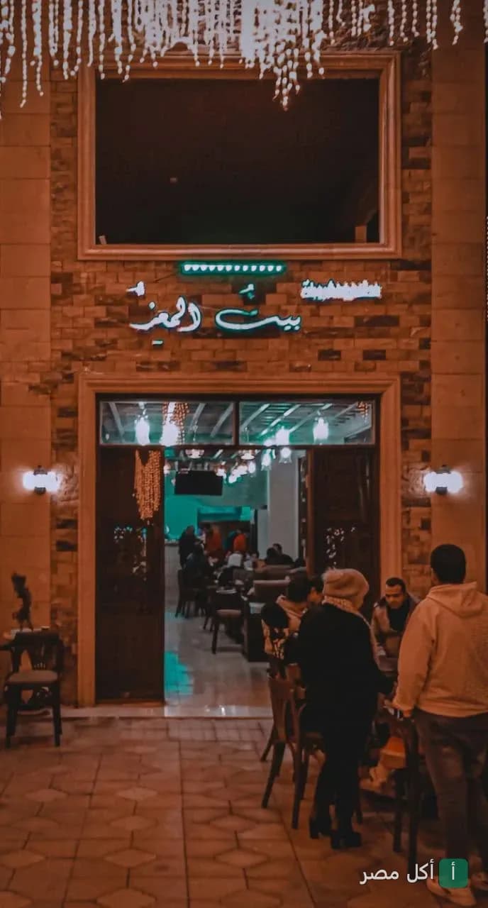 واجهة مطعم وكافيه بيت المعز في الجمالية ليلاً مع إضاءة دافئة وزوار يجلسون في الخارج.