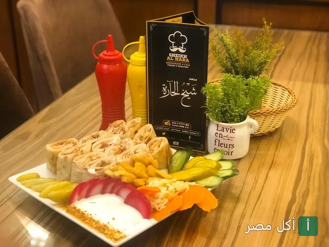 طبق شاورما مقطع مع مخللات وبطاطس محمرة بجانب قائمة طعام مطعم شيخ الحارة في الجمالية.