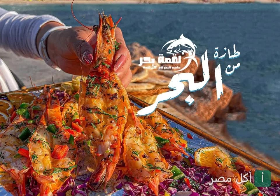 يد تمسك جمبري مشوي طازج على صينية مأكولات بحرية من مطعم لقمه بحر في سيدي جابر.