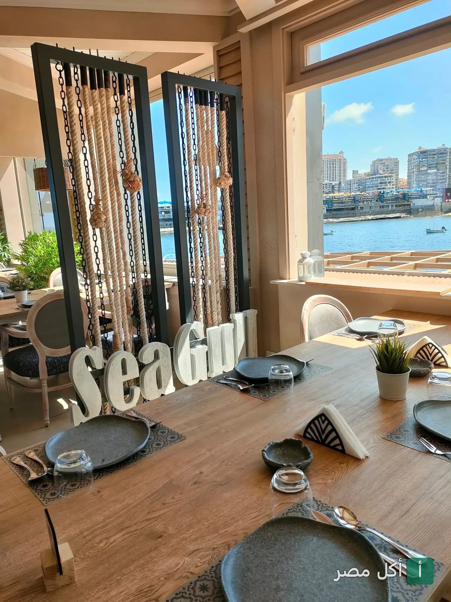 طاولات طعام خشبية مرتبة داخل مطعم سيجول المطل على البحر في سيدي جابر بالإسكندرية.