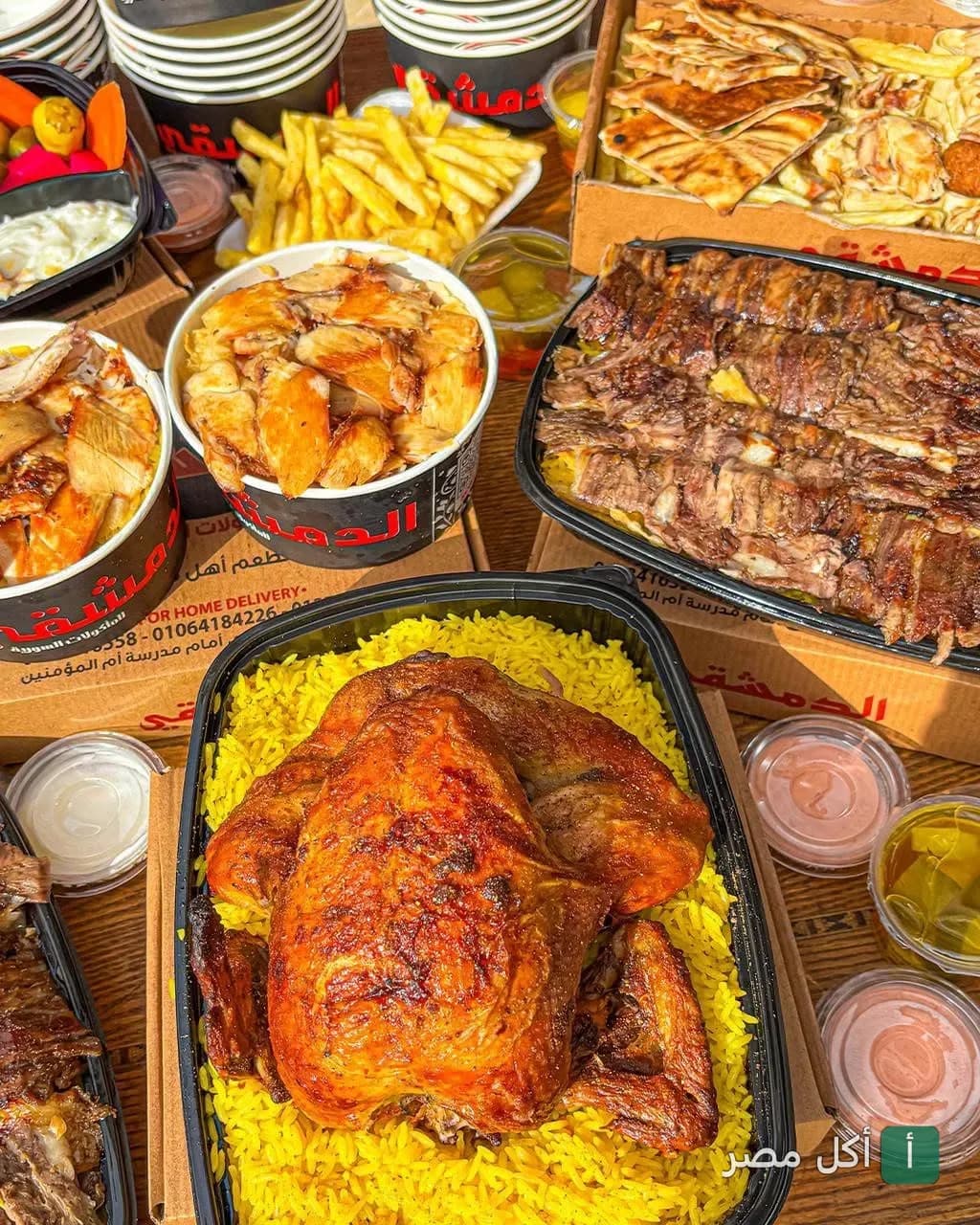 تشكيلة أطباق سورية من مطعم الدمشقي في طنطا تضم دجاج مشوي مع أرز، شاورما، وبطاطس مقلية.