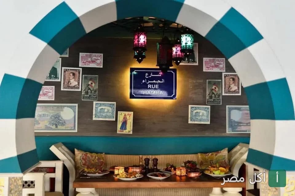 ديكور لبناني تقليدي في مطعم هايدا بالجيزة، يظهر قوس أزرق وأبيض مع فوانيس ملونة ولوحة شارع الحمراء.