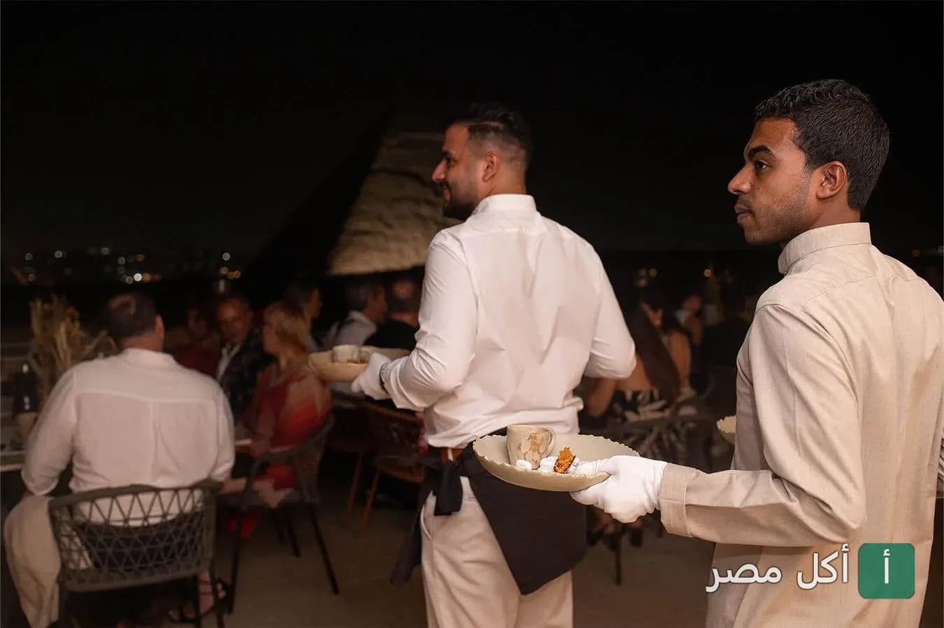نادل يرتدي زيًا رسميًا يقدم الطعام في مطعم خوفو بنزلة السمان في الجيزة ليلاً.