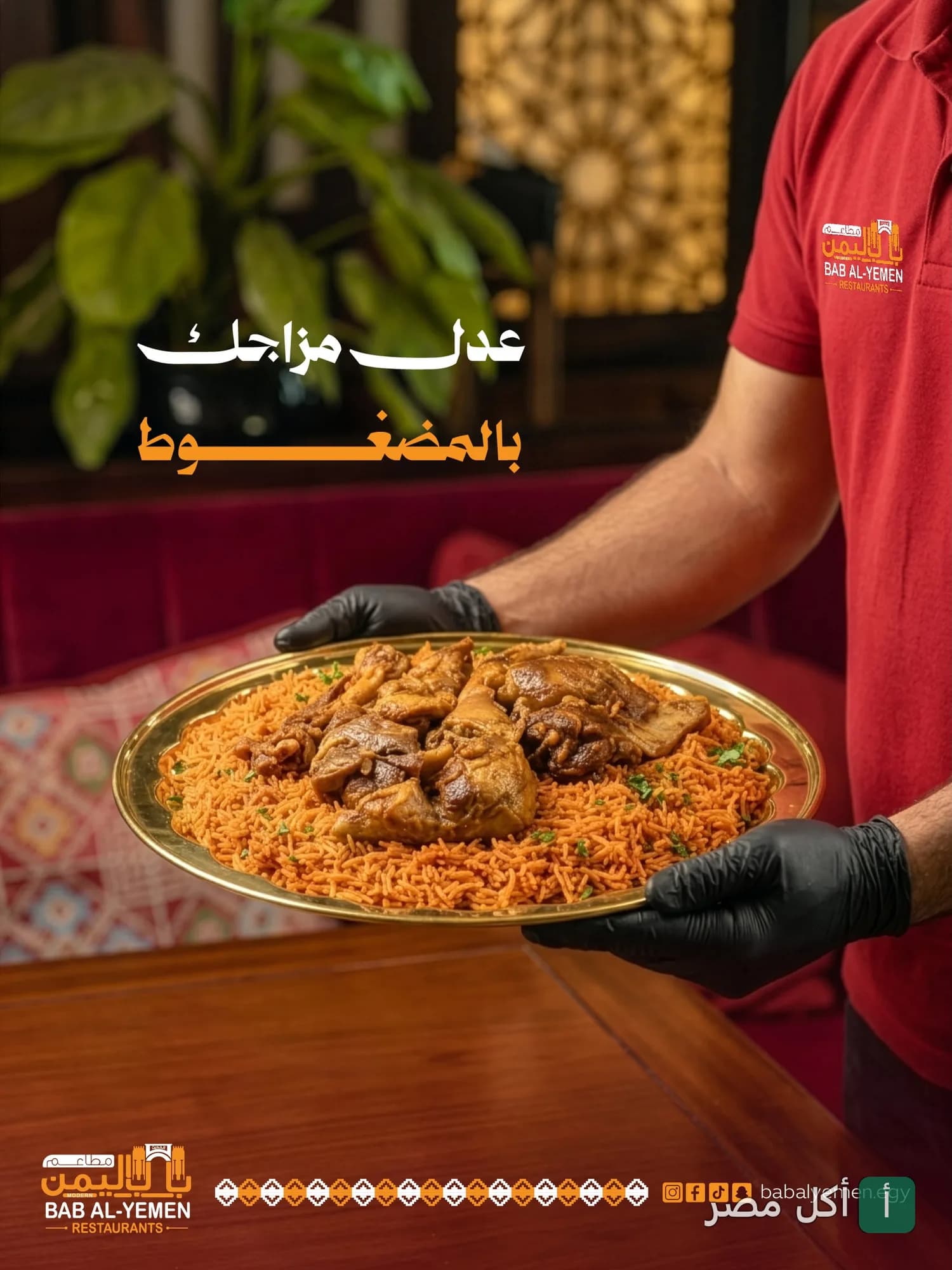 نادل يرتدي قفازات سوداء يقدم طبق مضغوط لحم مع أرز في مطاعم باب اليمن الحديث.